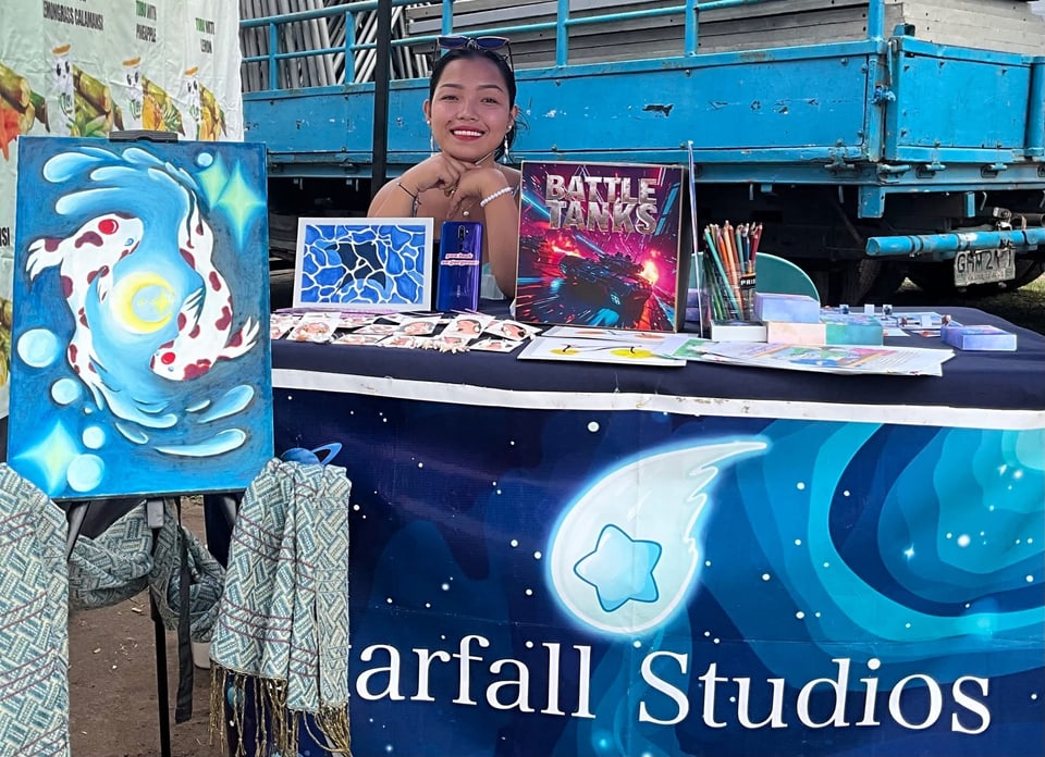 Paintings on easels beside the studio table at an outdoor event.