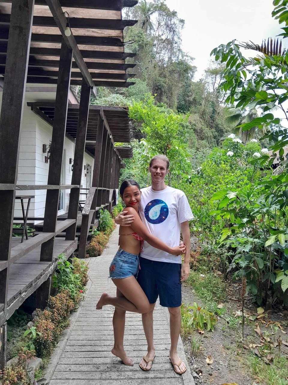 Two people on a garden path outside a wooden house.
