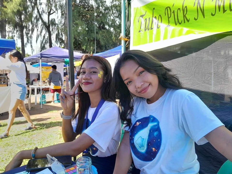 Two volunteers in studio shirts smile at a market booth.