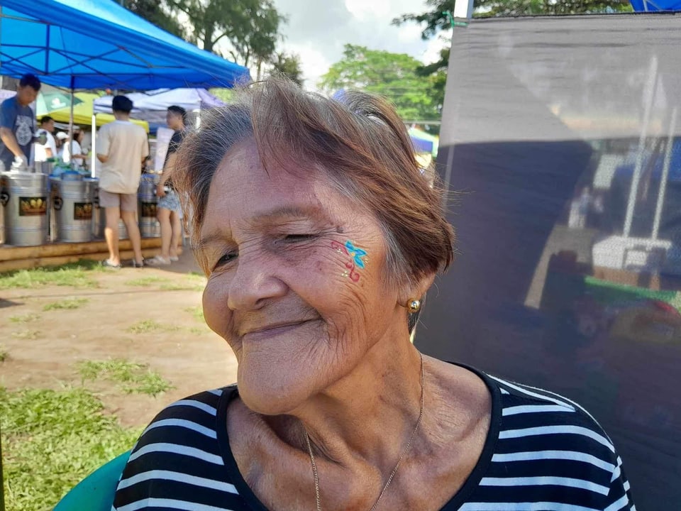 A woman with face paint smiles at an outdoor event.