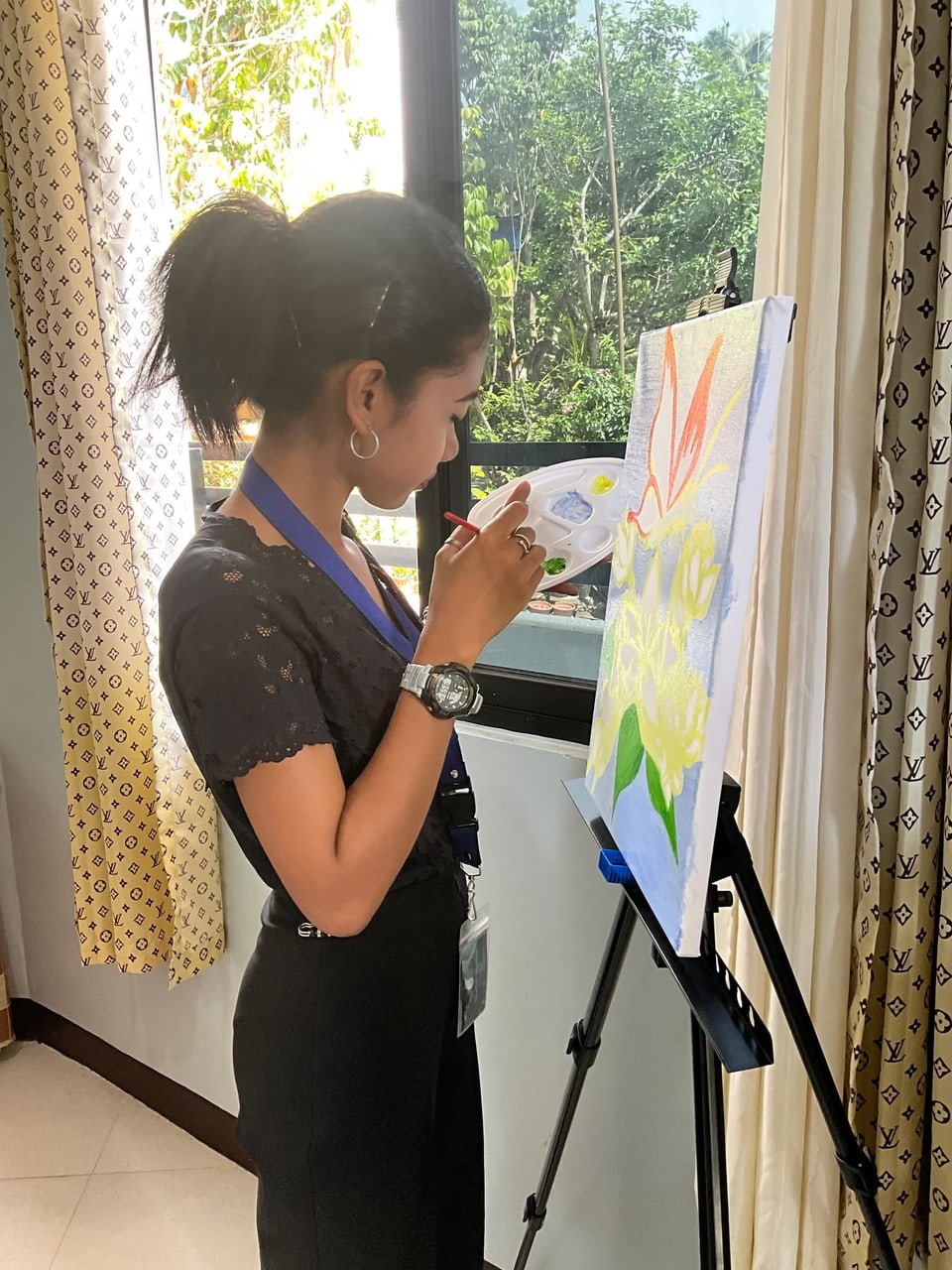A student paints at an easel by a window.