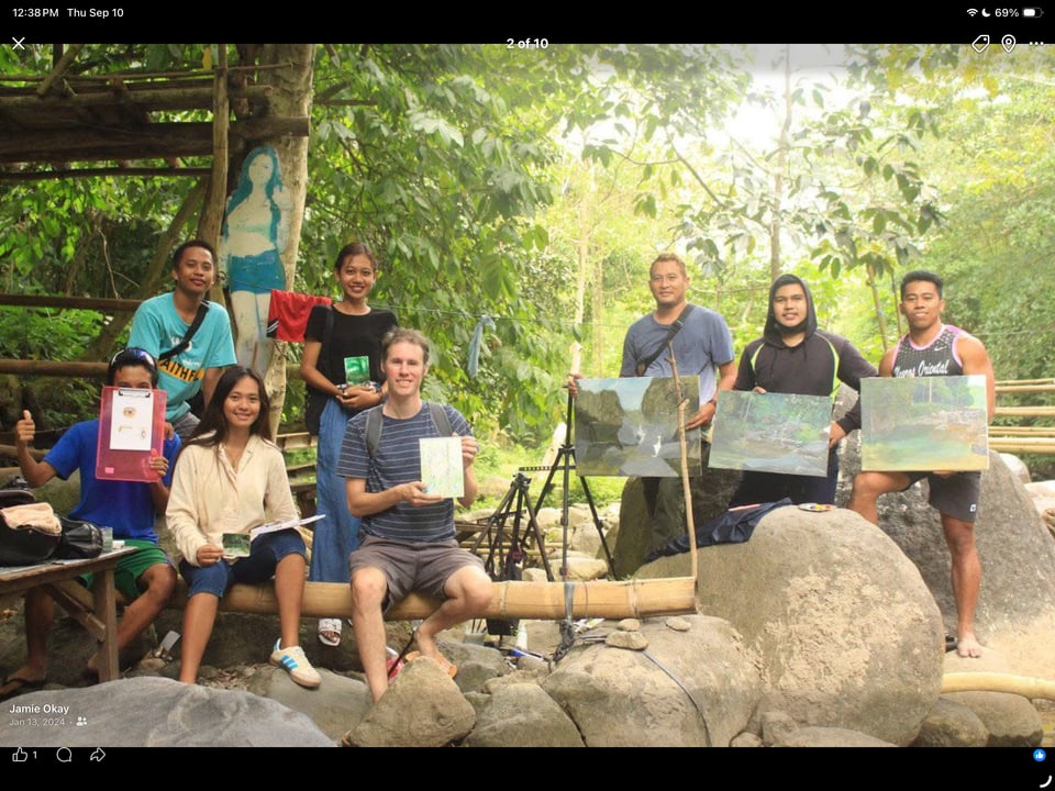 A group holds up their finished paintings at an outdoor painting session.