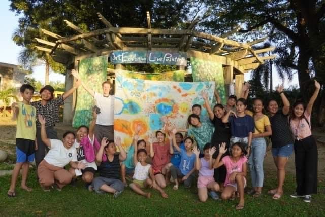 A large group of students and volunteers pose in front of a finished mural.